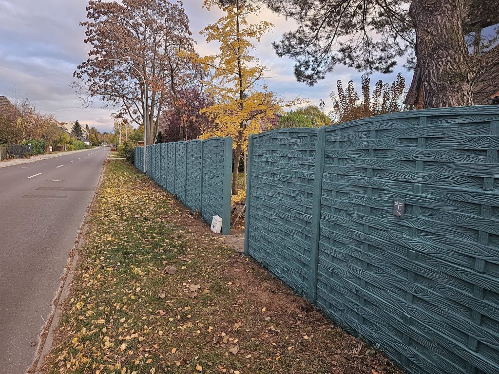 Grau gestrichener Betonzaun in Holzoptik entlang einer Straße