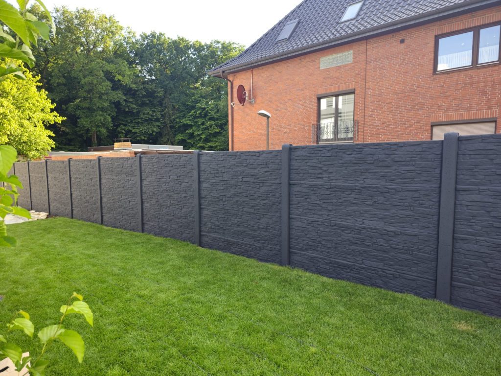 Dunkler Betonzaun mit Steinstruktur an einem gepflegten Garten