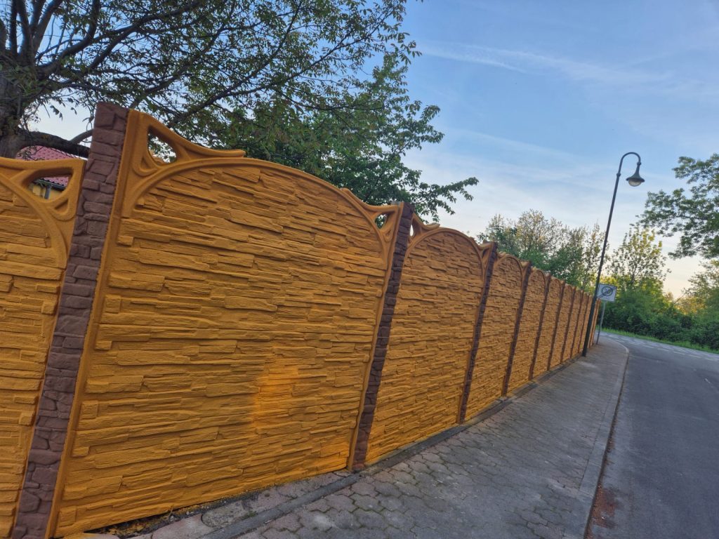 Ockerfarbener Betonzaun mit dekorativer Steinstruktur an einer Straße